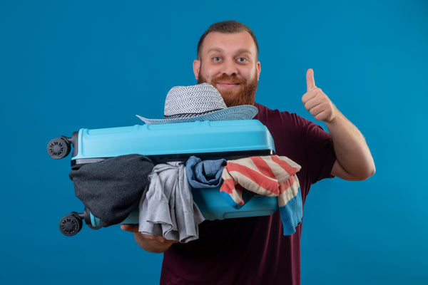Man holding a suitcase that has clothes spilling out of it and showing a thumbs up